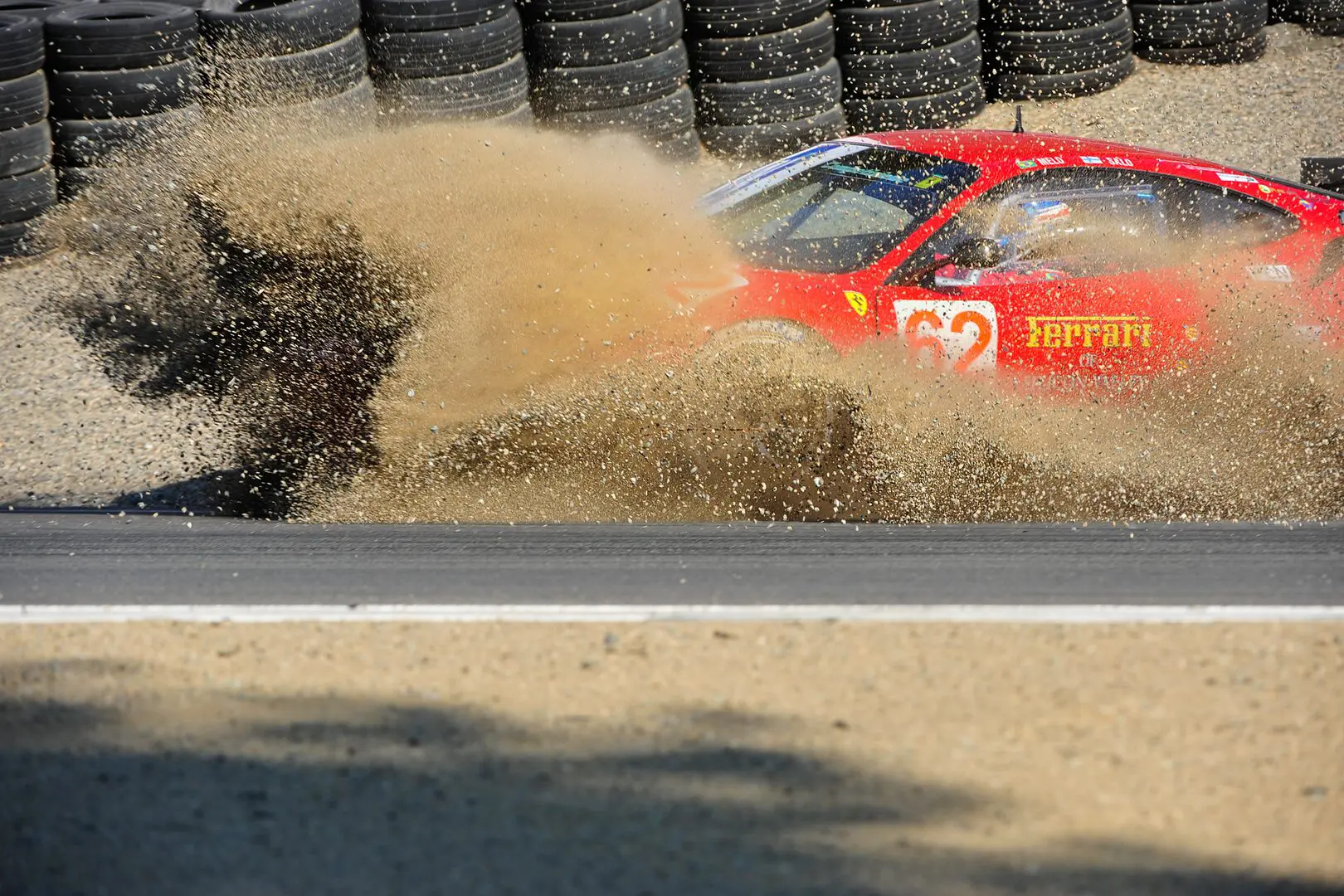 A red car is driving through the sand.