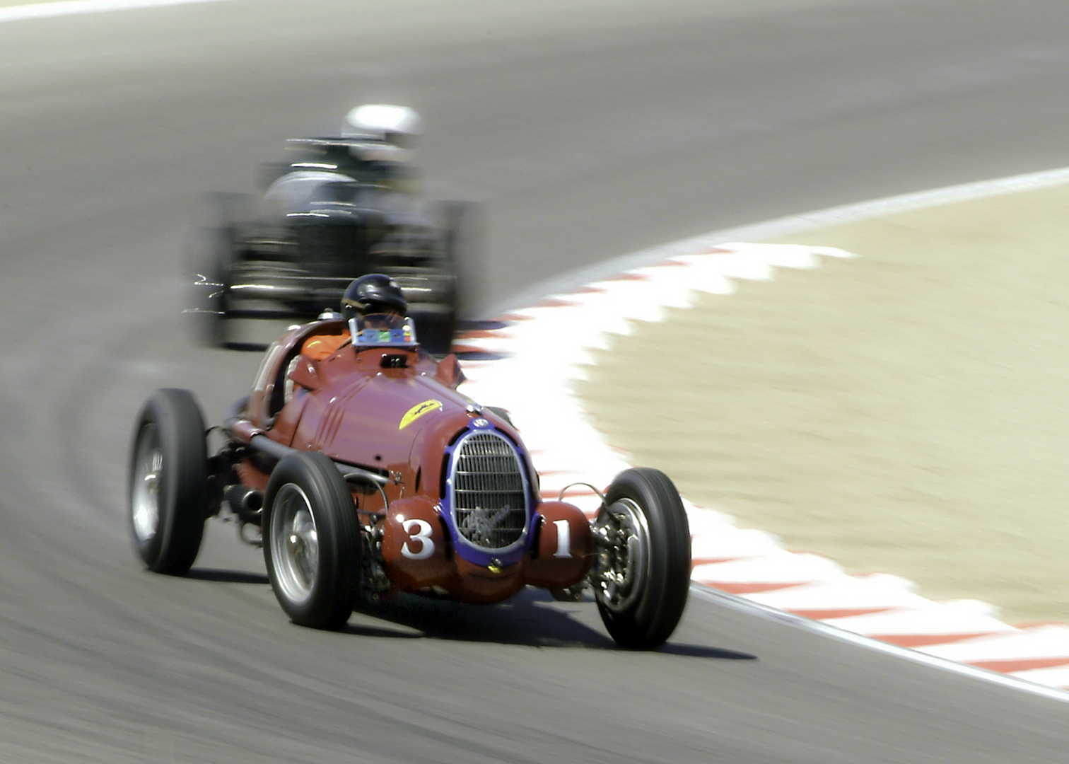 A race car driving down the track with another racing car behind it.